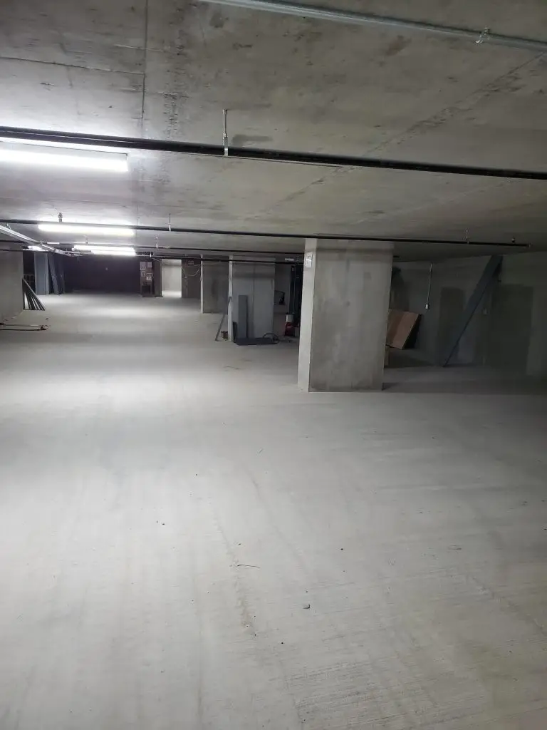 Pest control technician in safety vest placing a secured, tamper-proof rodent bait station in a multi-level commercial parking garage in downtown Seattle.
