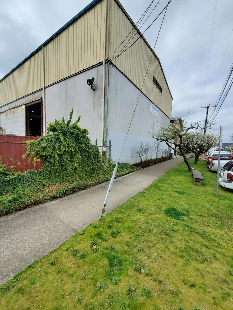 Pest control expert in high visibility gear surveying pallet racks and floor-level gaps for rodent activity in a Kent, WA industrial warehouse.